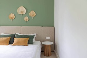 A bed with white bedding, multiple pillows, a round wooden side table, and a wall with four leaf-shaped wall art pieces. - Exclusive beachfront apartment (Belle Mare)