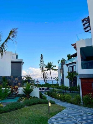 A modern building with a stone facade, a pathway leading to a seating area, and a view of the ocean.