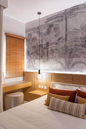 Un dormitorio con cama, almohadas, una mesita de noche, lámpara, ventana con persianas y un mural temático de naturaleza.
