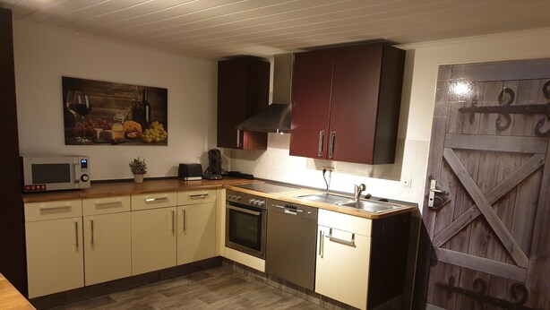 A kitchen with wooden cabinets, a microwave, a toaster, a sink, and a stove. - Appartement für 2 Personen in Ruhiger Lage (Ilsede)