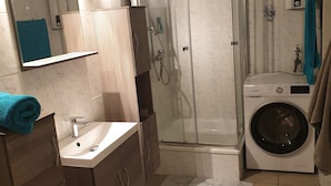 A modern bathroom with a glass-enclosed shower, a built-in sink, a washing machine, and a mirror above the sink. - Appartement für 2 Personen in Ruhiger Lage (Ilsede)