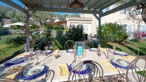 Enjoy a meal al fresco in a serene outdoor setting surrounded by lush greenery and a charming building in the background.