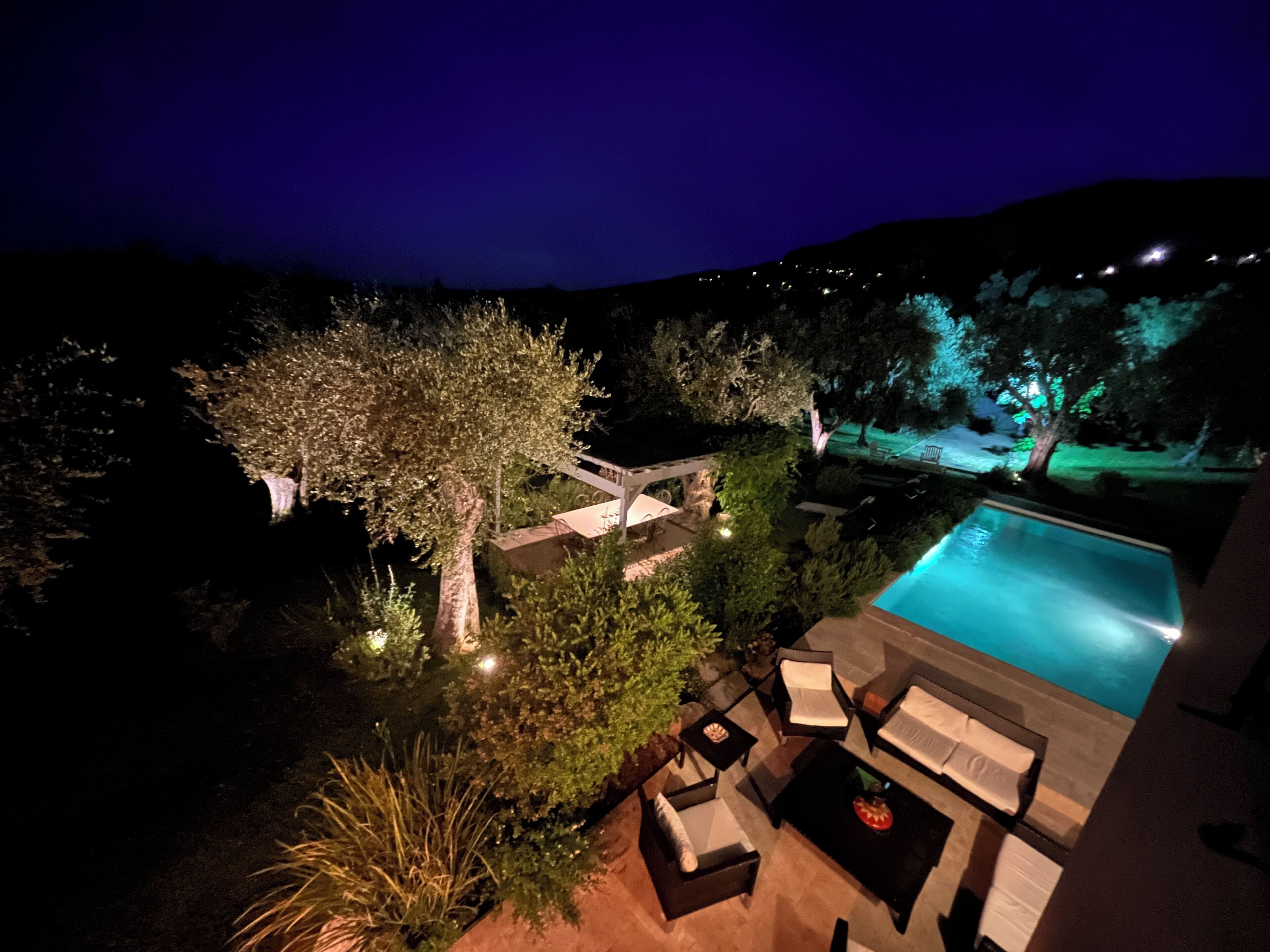 A nighttime view of a pool area with outdoor furniture and a tree.