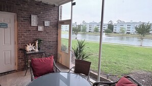 Um pátio com uma mesa redonda e cadeiras de vime, uma parede de tijolos e vista para um edifício através da água.