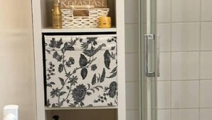 Une salle de bain avec un meuble blanc contenant des articles de toilette et un panier noir.