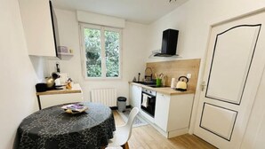Une cuisine compacte comprenant une table à manger, des chaises, une fenêtre, une cuisinière et une hotte noire.