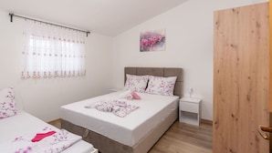 A bedroom with a bed, a bedside table, a nightstand, a wooden door, a window with curtains, and a wall-mounted painting. - Nice apartment for 4 people with WIFI, A/C, TV and terrace (Biograd Na Moru)