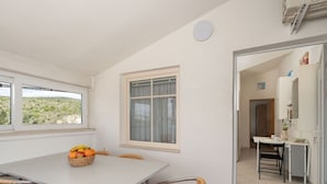 A dining area with a white table and wicker chairs, a fruit basket on the table, and a view of the outdoors through a window. - Nice apartment for 4 people with WIFI, A/C, TV and terrace (Biograd Na Moru)