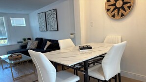 Uma sala de jantar com mesa de mármore branco, estrutura de metal preto e cadeiras estofadas em branco.