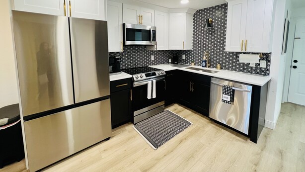 Uma cozinha moderna com armários brancos, eletrodomésticos de aço inoxidável, um painel de backsplash estampado e um tapete preto e branco.