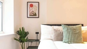 A bedroom with a bed, pillows, a plant, a desk, and a wall-mounted picture. - Stylish Flat, Ideal for Business & Long-Term Stays (Liverpool)