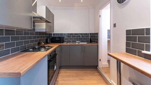 A compact kitchen with grey cabinets, a black microwave, and a wooden countertop. - Stylish Flat, Ideal for Business & Long-Term Stays (Liverpool)