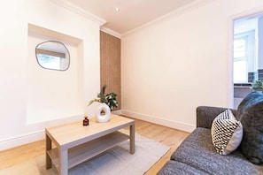 A modern living room with a wooden coffee table, a grey sofa, and a mirror on the wall. - Stylish Flat, Ideal for Business & Long-Term Stays (Liverpool)