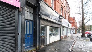 A storefront with a closed shutter, a blue door, and a sign for 'The Directors Guild'. - Stylish Flat, Ideal for Business & Long-Term Stays (Liverpool)