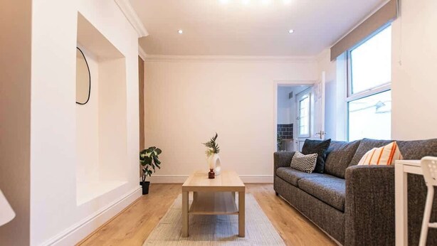 A modern living room with a wooden floor, a grey sofa, a white armchair, and a small wooden coffee table with a plant. - Stylish Flat, Ideal for Business & Long-Term Stays (Liverpool)