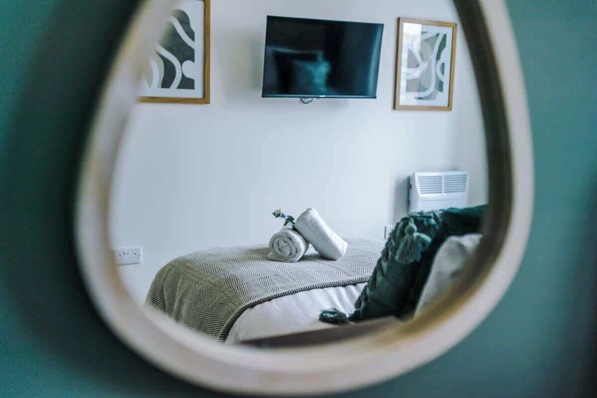 Een slaapkamer met een bed, een aan de muur bevestigde televisie en een lijst met een foto boven het bed.
