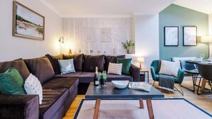 Ein modernes Wohnzimmer mit einem dunkelbraunen Sofa, einem Couchtisch mit einer Zeitschrift und einem grünen Sessel.