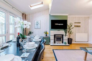 Un salon moderne comprenant un coin repas, une cheminée et un téléviseur fixé au mur.