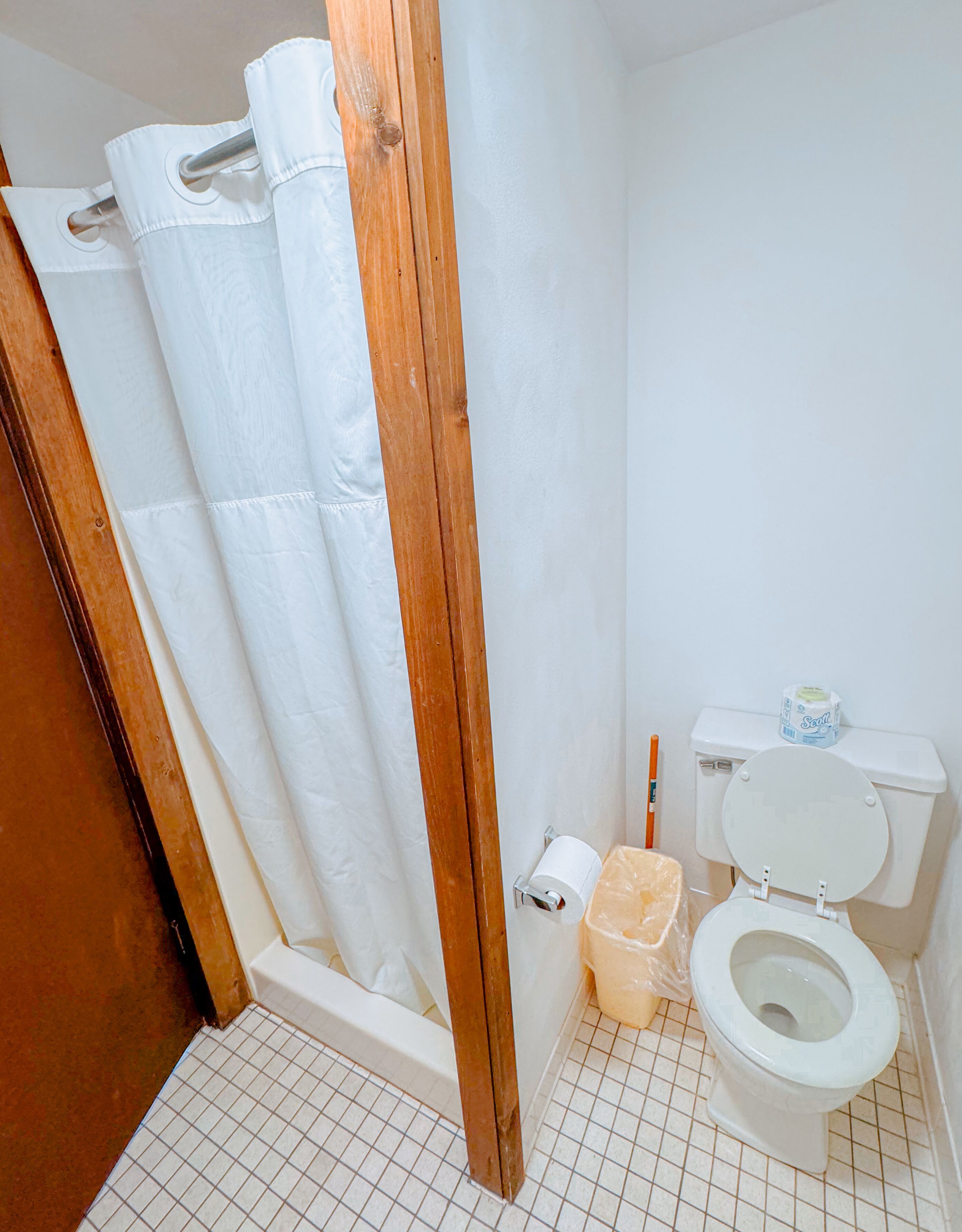 Un baño con cortina de ducha, inodoro y un rollo de papel higiénico.