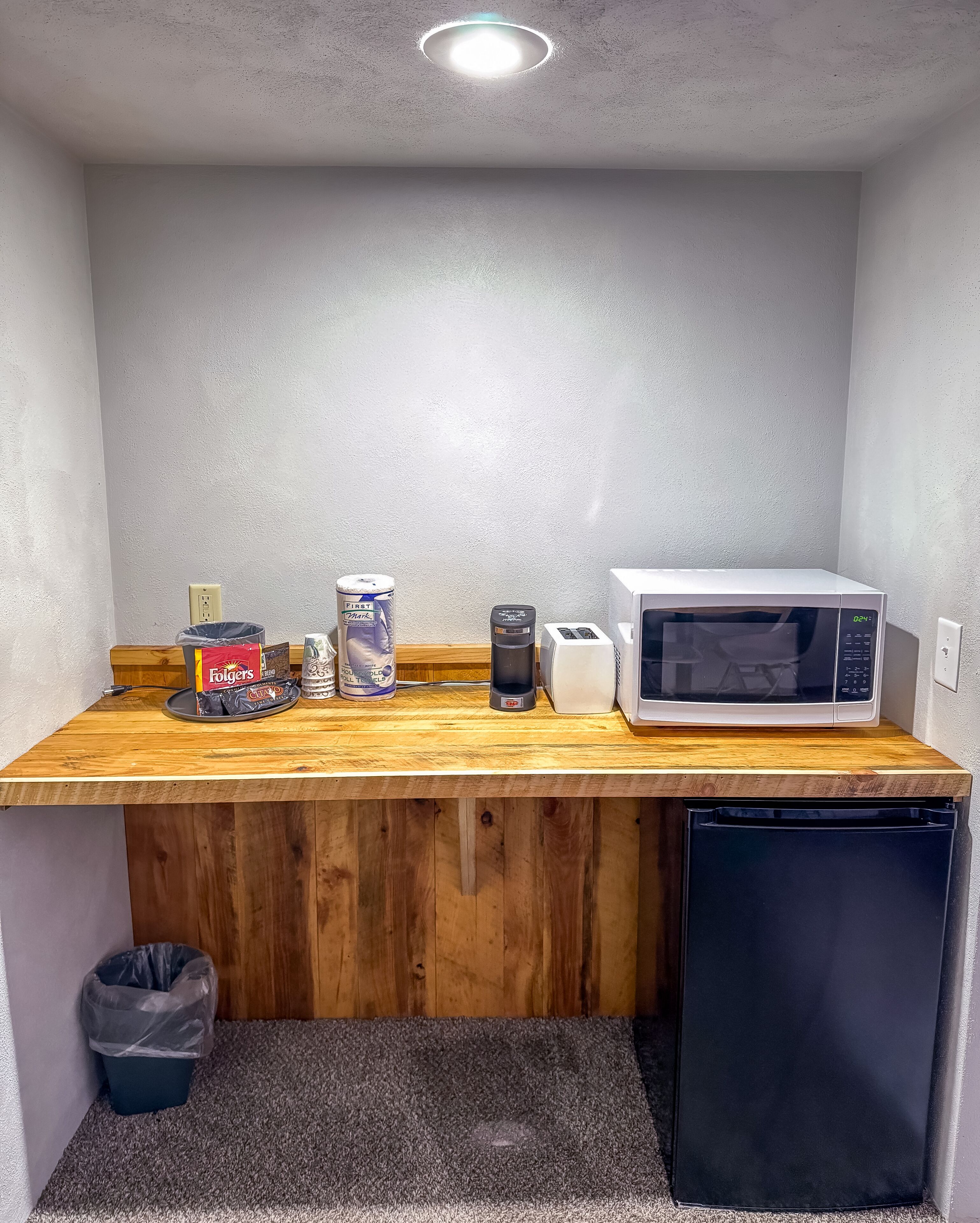 Una cocina compacta con encimera de madera, microondas, tostadora y cubo de basura.