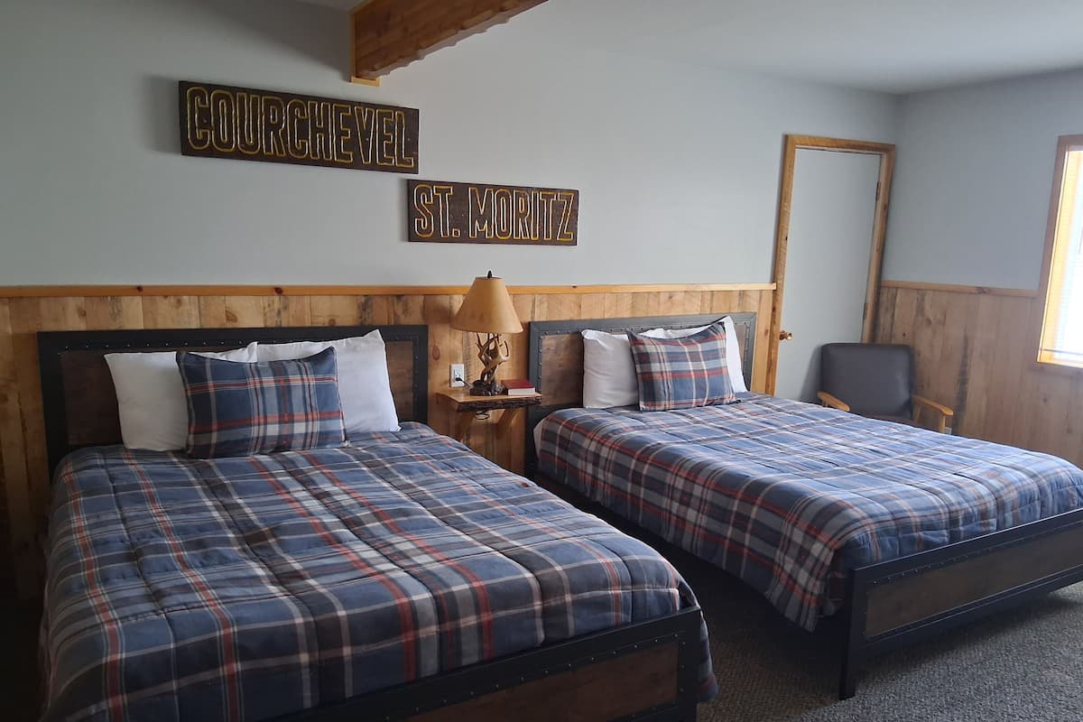 A room with two beds, a wooden headboard, a nightstand with a lamp, and a sign above the beds.