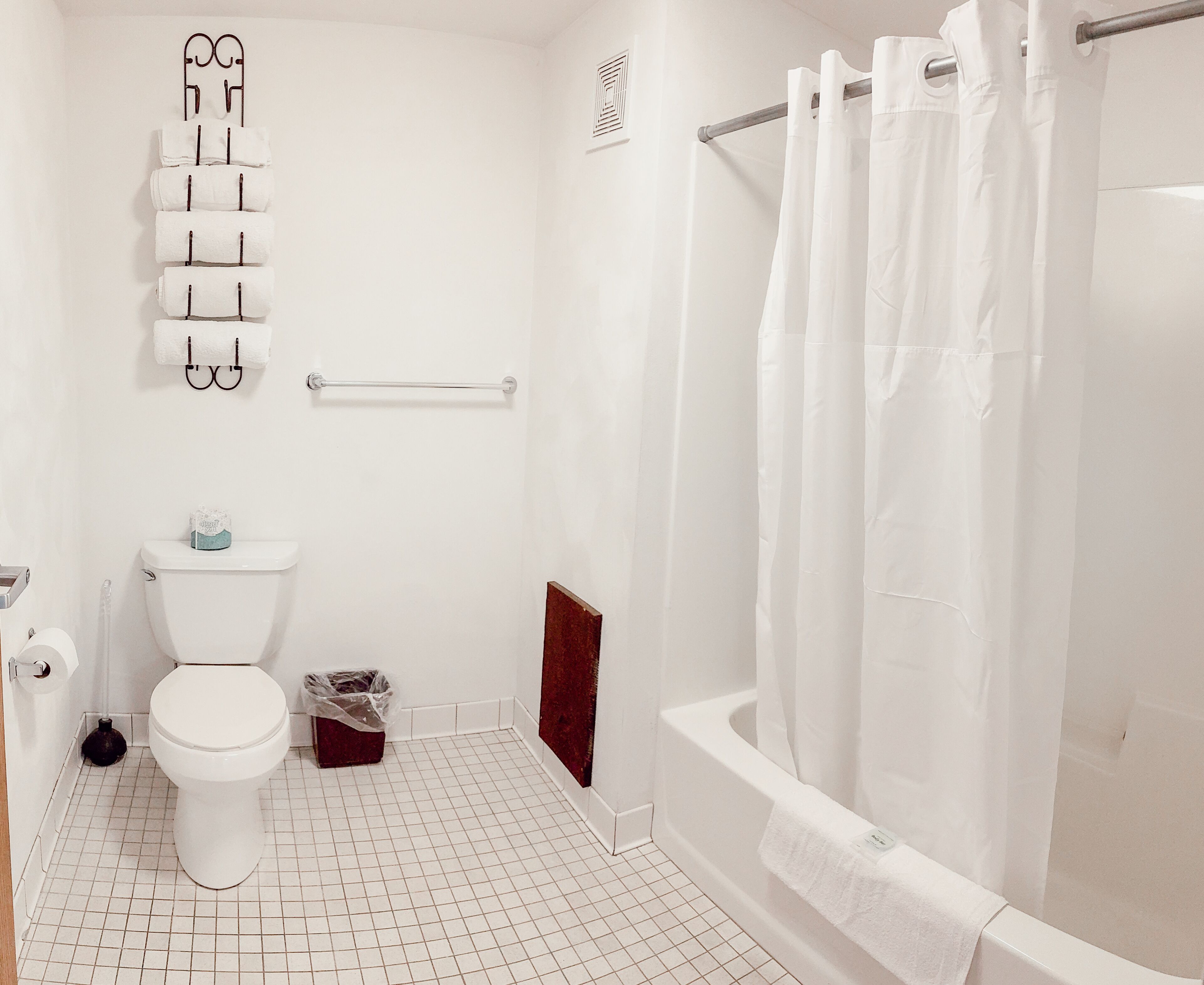 Casa de banho com sanita, chuveiro com cortina, porta-toalhas e suporte para papel higiénico.