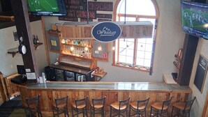 Zona de bar con mostrador de madera, varios taburetes y un televisor montado en la pared.