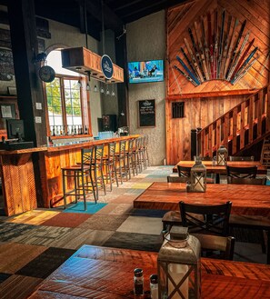 Un restaurante con zona de bar, mesas y sillas de madera. Una gran pared de madera exhibe varios esquíes.