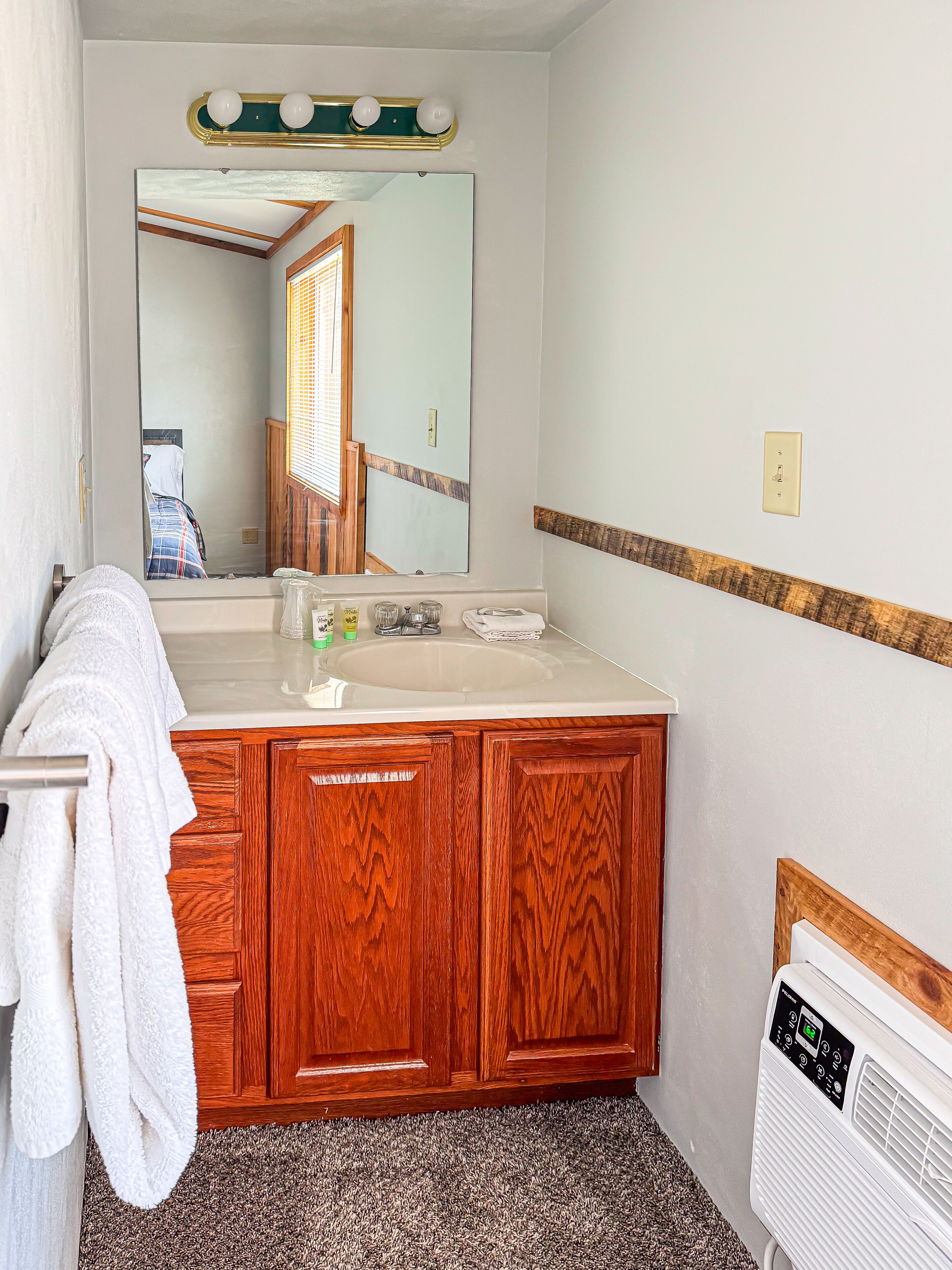 Une salle de bain avec des meubles en bois, un lavabo blanc et un miroir avec des lumières au-dessus.