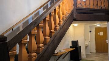 Un escalier avec des balustrades en bois et un lustre, menant à une pièce dotée d’une moquette verte et d’un petit tabouret.