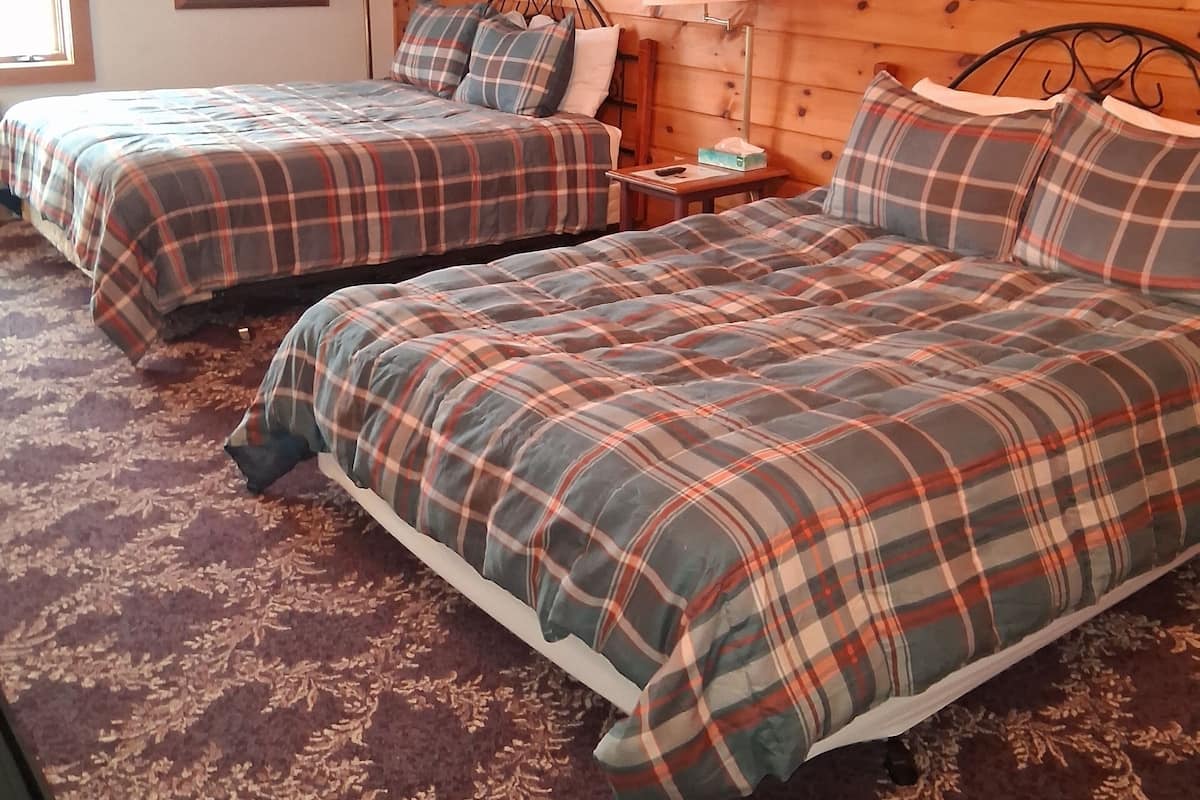 A cozy room with two beds, each with plaid bedding, a nightstand with a lamp, and a painting on the wall.