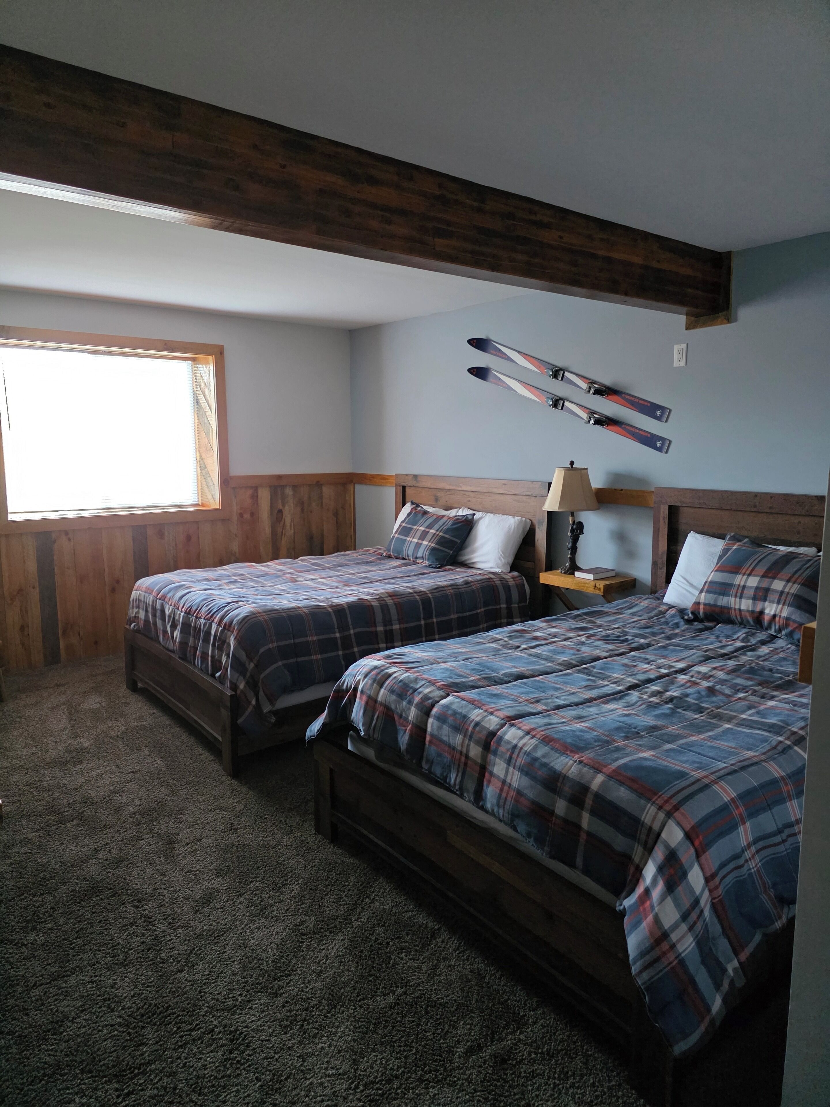Ein Schlafzimmer mit zwei Betten, einem Fenster, Holzbalken und Skiern an der Wand.