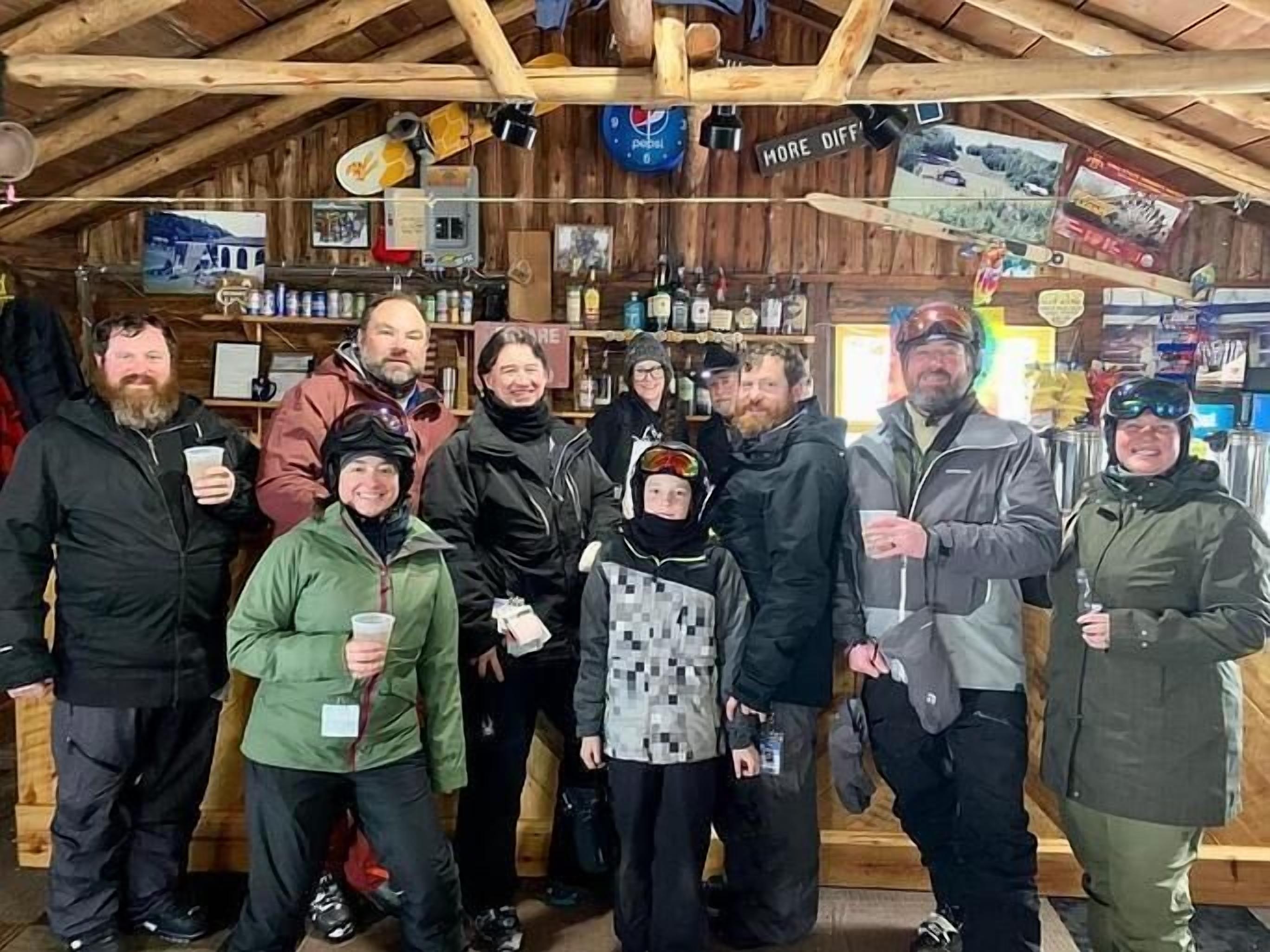 A group of people in a rustic wooden room with shelves stocked with various items, including bottles and a sign that reads "MORE DIFF."