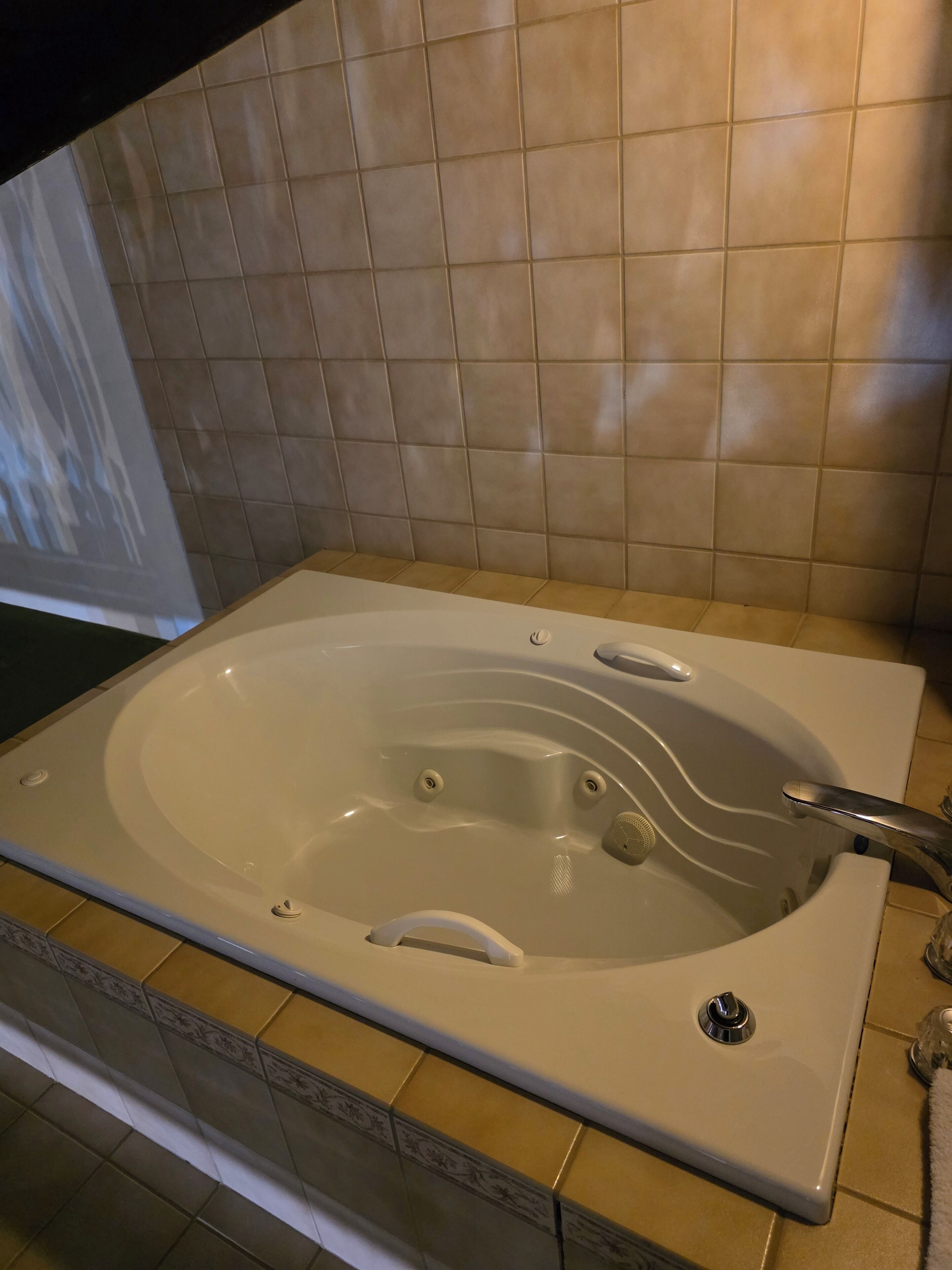 Uma banheira de hidromassagem retangular com uma única torneira e ralo, em frente a uma parede revestida de azulejos.