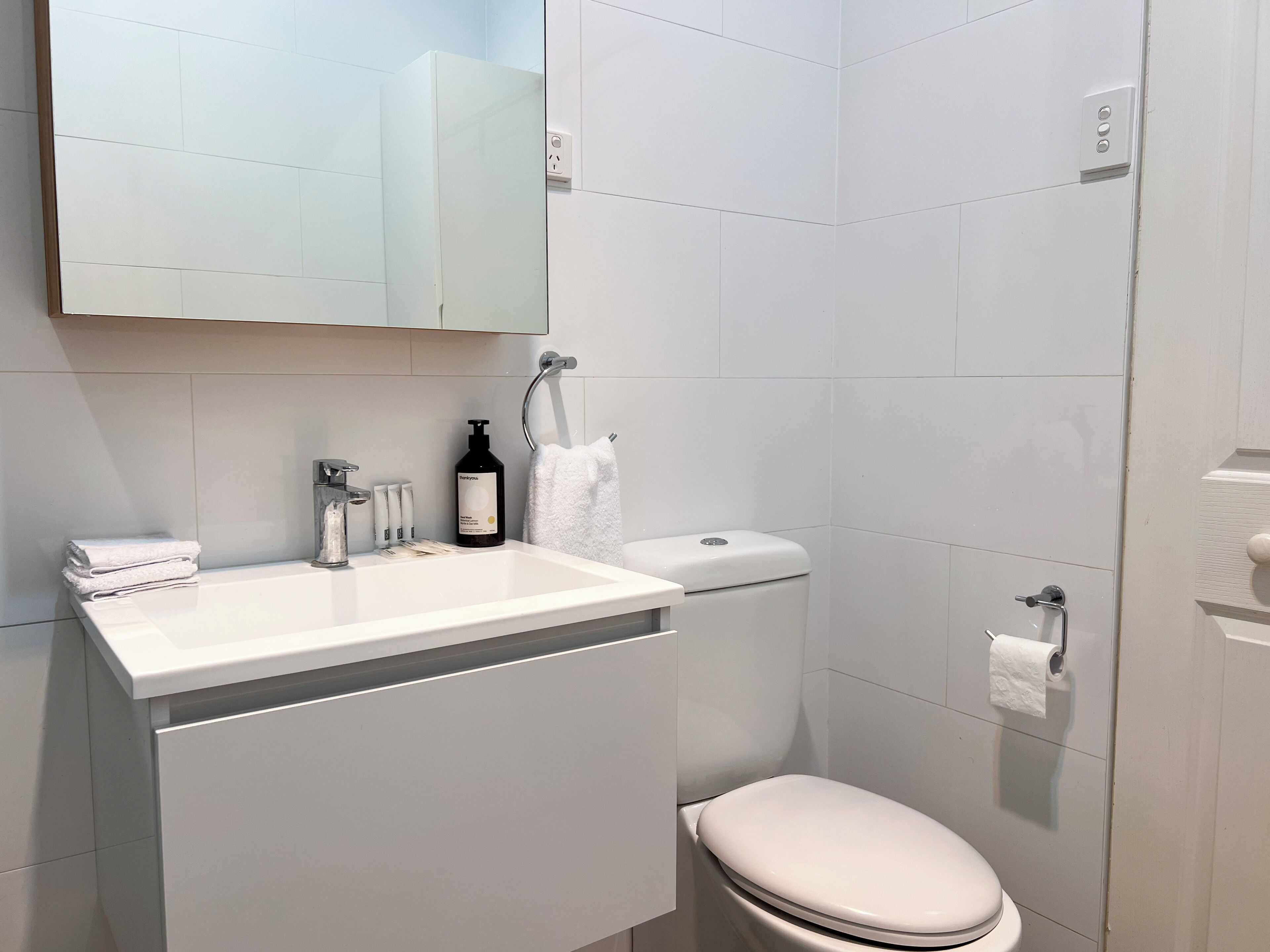 A modern bathroom with a white sink, a toilet, and a mirror above the sink.