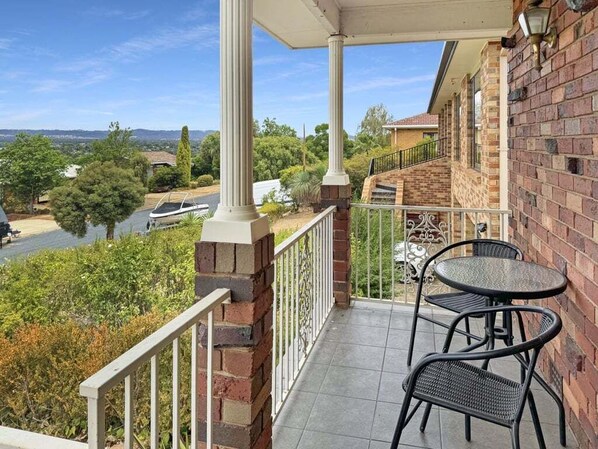 A balcony with two chairs and a table, overlooking a river and greenery.