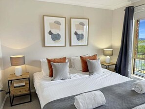 A hotel room with a bed, two bedside tables, a window with curtains, and artwork on the wall.