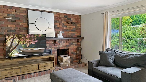 Un salon avec une cheminée en briques, un canapé gris et un téléviseur à écran plat posé sur un meuble en bois.