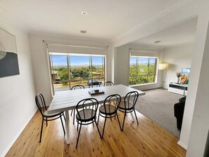 A spacious room with a large dining table and chairs, large windows offering a view of the outdoors, and a modern interior design.
