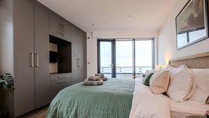 Ein modernes Schlafzimmer mit einem großen Bett, einem grauen Kleiderschrank und einem Balkon mit Blick.