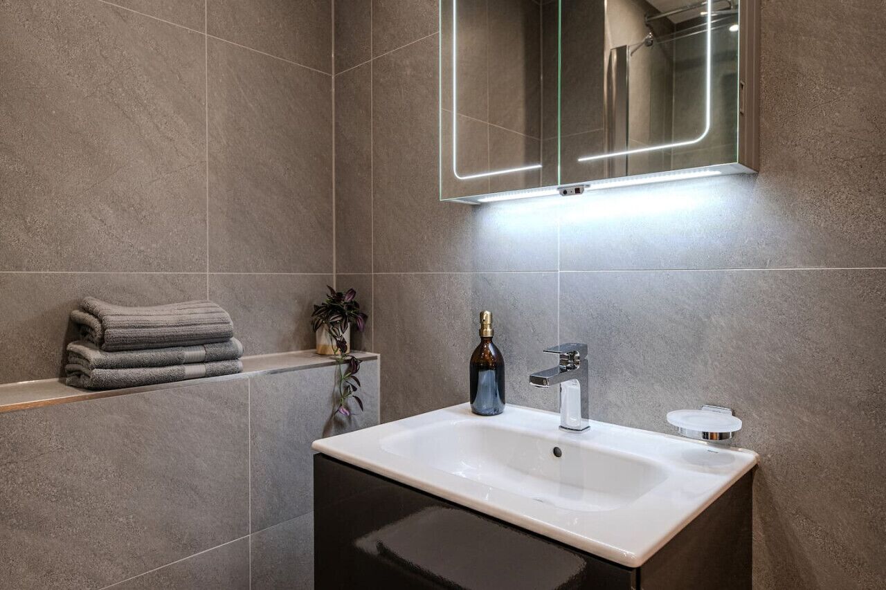 Une salle de bain moderne avec un grand miroir, un lavabo blanc et un porte-serviettes.