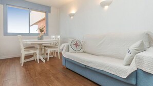 Een moderne woonkamer met een witte bank, een eettafel met stoelen en een groot raam met uitzicht op een bakstenen gebouw.