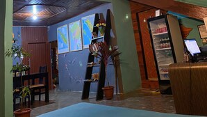 A hotel lobby with a high ceiling, exposed wooden beams, a seating area with a sofa and chairs, a small table, and a staircase leading to an upper level. - Second Hope Lodge (Padang)