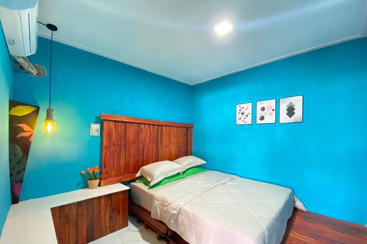A bedroom with a wooden bed, a nightstand, a wall-mounted air conditioner, and three framed pictures.