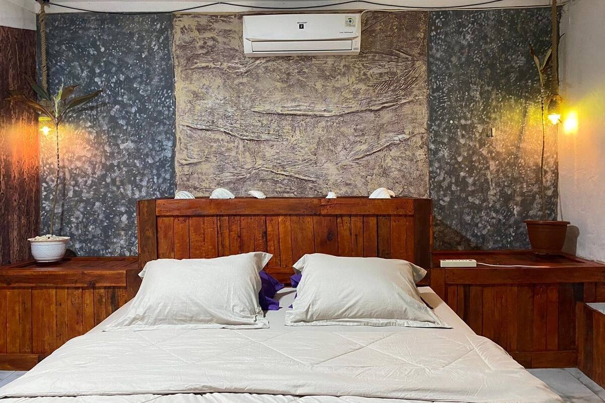 A bedroom with a wooden headboard, a large tapestry, and a wall-mounted air conditioner.