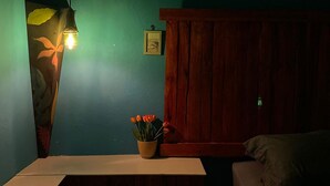 A bedroom with a wooden headboard, a bedside table with a vase of flowers, and a hanging light fixture. - Second Hope Lodge (Padang)