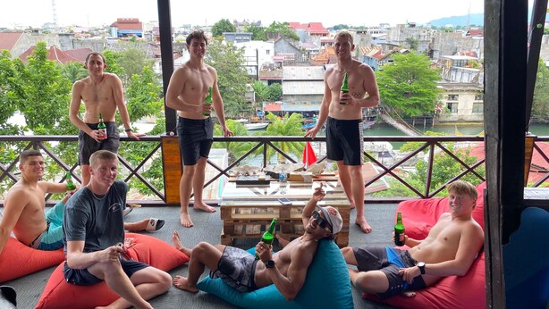 A group of people on a balcony with a view of a cityscape, some holding bottles. - Second Hope Lodge (Padang)