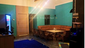 A cozy room with a brown sofa, wooden chairs, a small table, and a TV. - Second Hope Lodge (Padang)