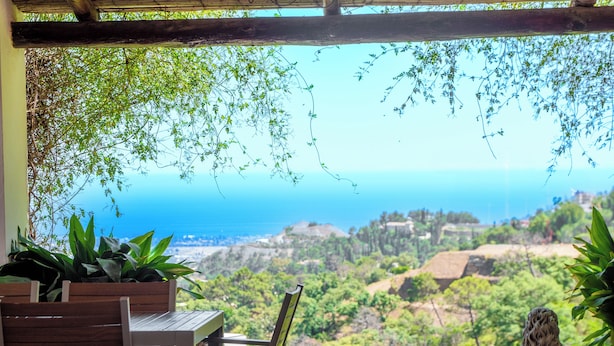 Pátio com mesa e cadeiras, oferecendo uma vista panorâmica da paisagem costeira, com vegetação e edifícios.