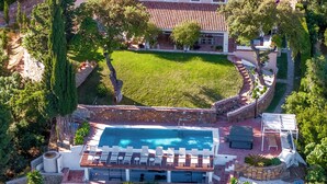 Uma casa grande com piscina, rodeada por um jardim bem cuidado e árvores.